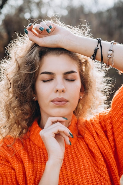 Une jeune fille bouclée dans un pull orange sur le fond de la nature d'automne