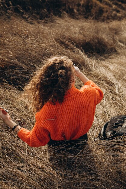 Une jeune fille bouclée dans un pull orange sur le fond de la nature d'automne