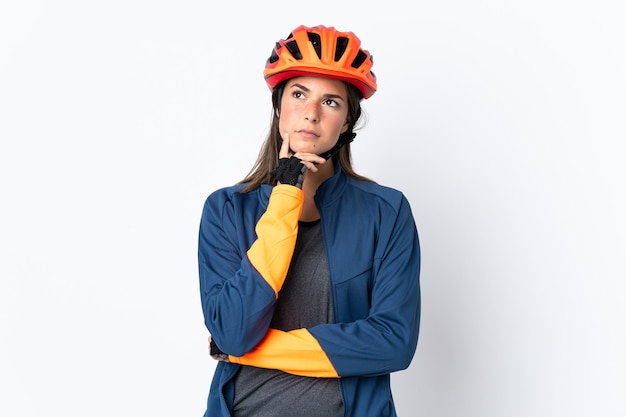 Jeune fille brésilienne cycliste isolée sur un mur blanc ayant des doutes tout en levant les yeux