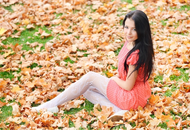 Jeune fille brune assise sur les feuilles d'automne