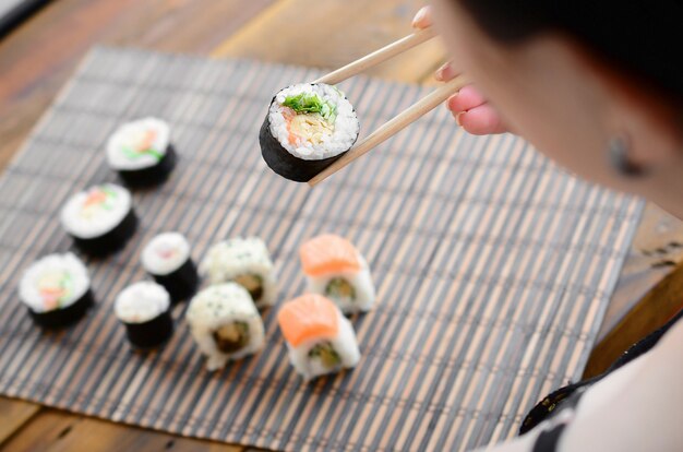 Jeune fille brune avec des baguettes est titulaire d&#39;un rouleau de sushi sur un fond de tapis de serwing en paille de bambou.