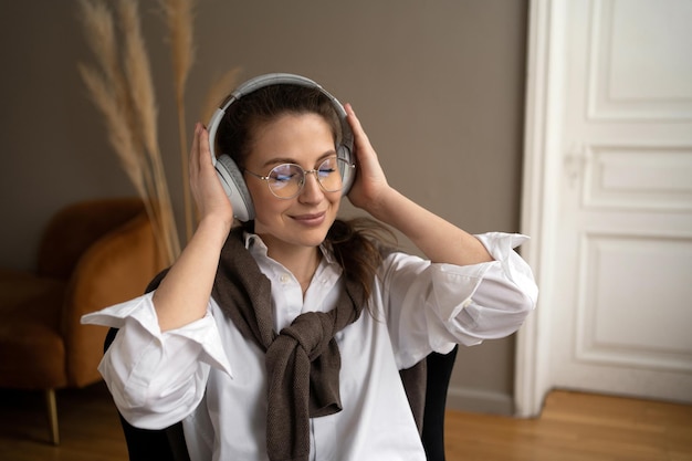 Une jeune fille brune calme et paisible dans une chemise blanche écoute de la musique ou un livre audio avec un casque