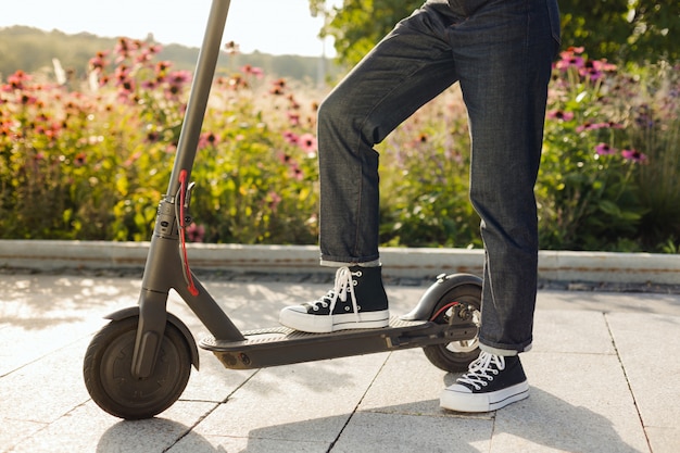 Jeune fille brune chevauchant un trottinette électrique écologique dans un parc par temps ensoleillé sur les trottoirs