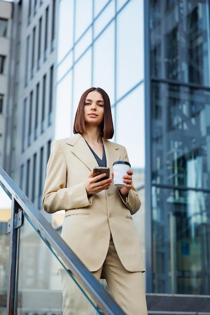 Une jeune fille brune dans le contexte d'un centre d'affaires centre de bureau Portrait d'une startup réussie Smartphone café costume décontracté