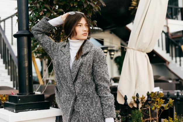 Jeune fille brune dans un manteau gris tendance se promenant dans les rues de la ville en profitant du temps