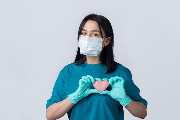 Une jeune fille brune dans un masque médical protecteur tient un coeur rose, symbolise la vie. Notion de coronavirus.