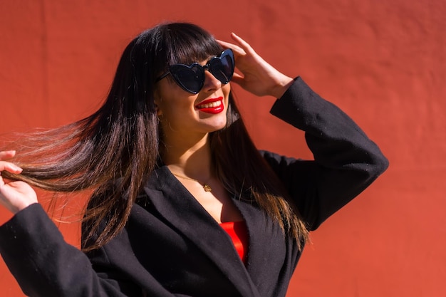 Jeune fille brune dans un portrait sur fond rouge avec des lunettes de coeurs valentine souriant