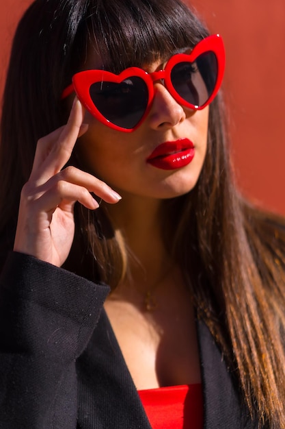 Jeune fille brune sur fond rouge avec des lunettes de coeurs Saint Valentin portrait de jolie fille