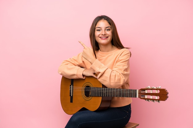 Jeune fille brune avec une guitare isolée pointant sur le côté pour présenter un produit