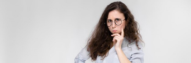 Jeune fille brune à lunettes. La fille mit un doigt sur sa joue.