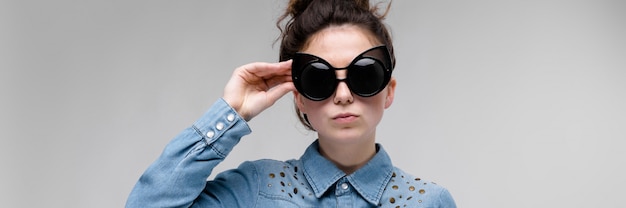 Jeune fille brune à lunettes noires. Lunettes de chat. Les cheveux sont rassemblés en un chignon. La fille ajuste sa chemise et ses lunettes.