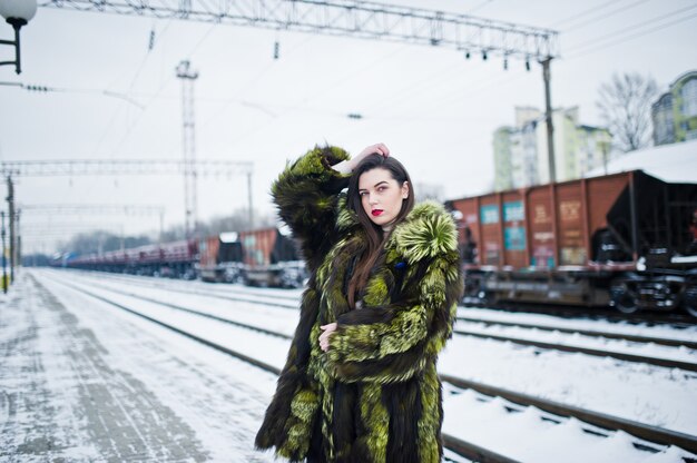 Jeune fille brune en manteau de fourrure vert sur la station de plate-forme au jour de l'hiver.