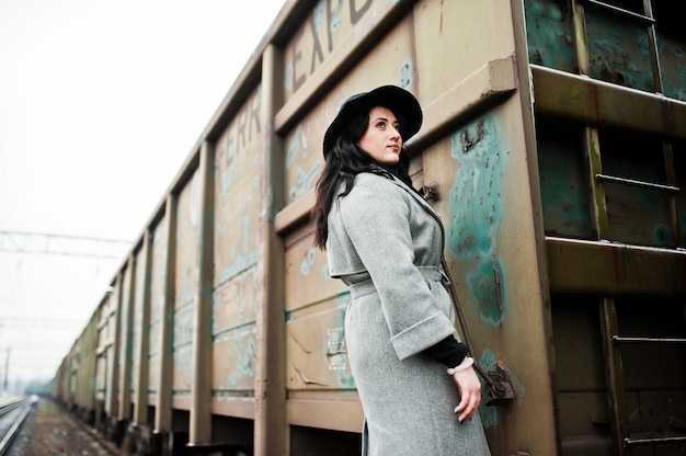 Jeune fille brune en manteau gris avec un chapeau dans la gare