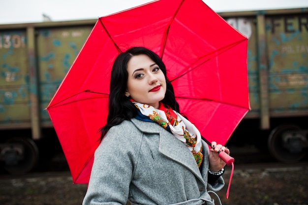 Jeune fille brune en manteau gris avec un parapluie rose dans la gare