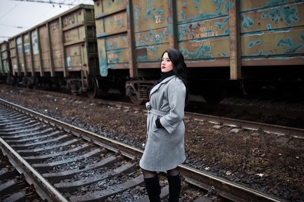 Jeune fille brune en manteau gris posée dans une gare