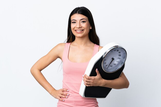 Jeune fille brune sur mur blanc isolé avec machine de pesage