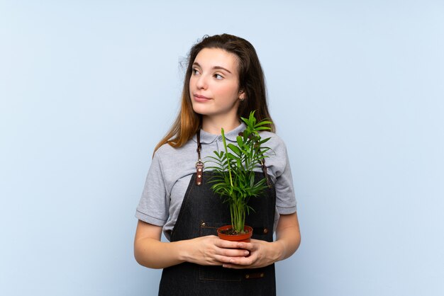 Jeune fille brune sur un mur bleu isolé, prenant un pot de fleurs