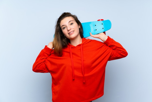 Jeune fille brune sur un mur bleu isolé avec skate