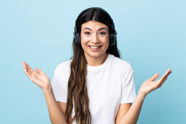 Jeune fille brune sur mur bleu isolé surpris et écouter de la musique