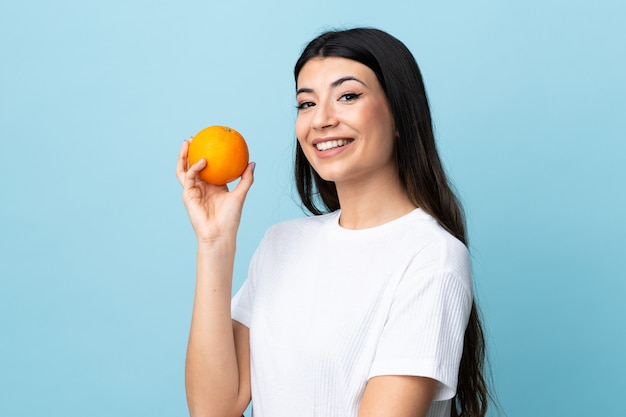 Jeune fille brune sur mur bleu tenant une orange