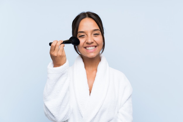 Jeune fille brune en peignoir avec maquillage sur mur bleu isolé