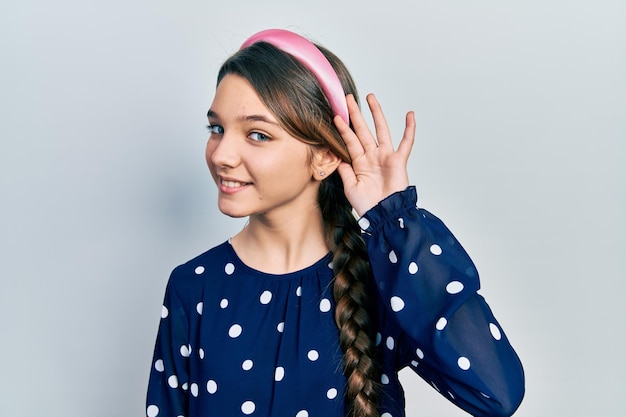 Jeune fille brune portant un look élégant souriant avec la main sur l'oreille en écoutant une rumeur ou un concept de surdité de commérages