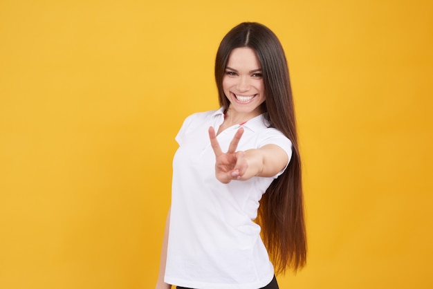 Jeune fille brune pose avec le signe de la victoire isolé.