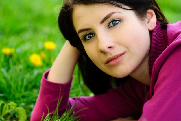 Jeune fille brune prendre du plaisir sur l'herbe avec des pissenlits, portrait en plein air. Gros plan du visage