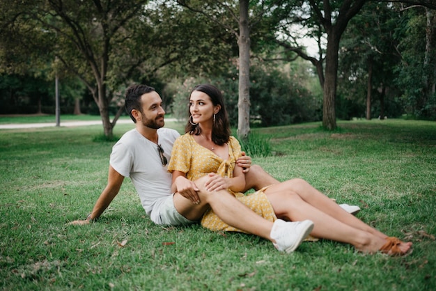 Une jeune fille brune en robe jaune est assise entre les jambes de son petit ami sur l'herbe dans la vieille ville d'Espagne. Un couple de touristes en train de rire lors d'un rendez-vous dans le parc valencien.