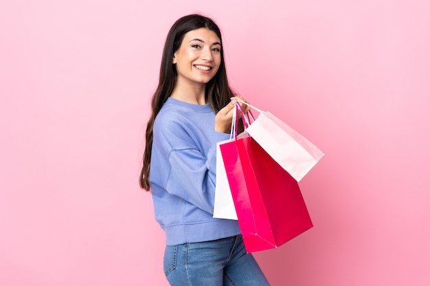 Jeune fille brune sur rose isolé tenant des sacs à provisions et souriant
