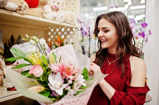 Jeune fille brune en rouge acheter des fleurs au magasin de fleurs.