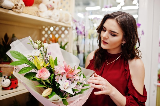 Jeune fille brune en rouge acheter des fleurs au magasin de fleurs