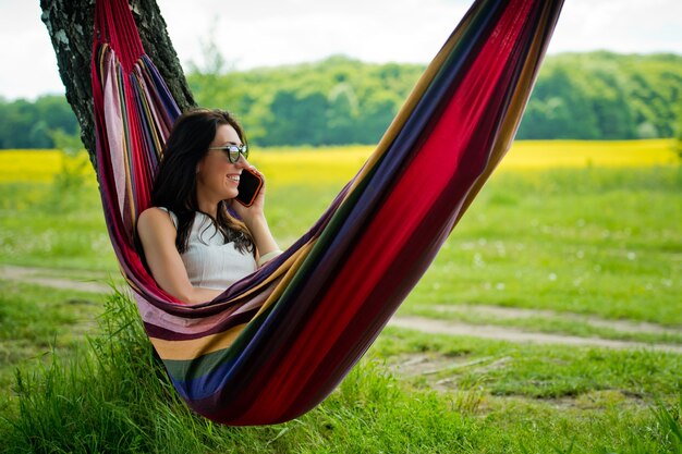 Jeune fille brune se trouve dans un hamac et parle sur le téléphone mobile.