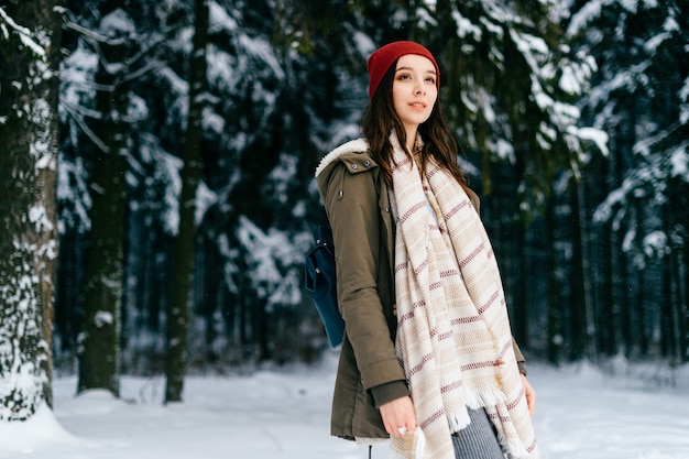 Jeune fille brune séduisante avec un foulard chaud posant dans la forêt de neige