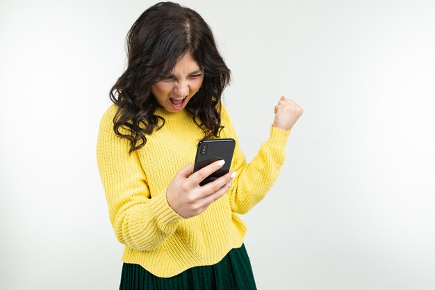 Jeune fille brune souriante regardant l'écran du smartphone sur un studio blanc