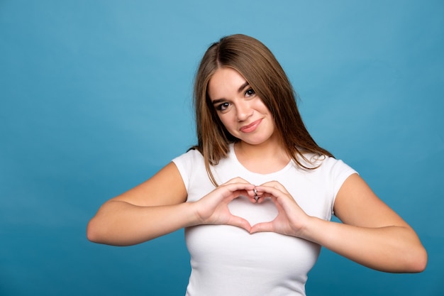 Jeune fille brune en t-shirt blanc montrant entendre signe à l'aide des mains, fond bleu