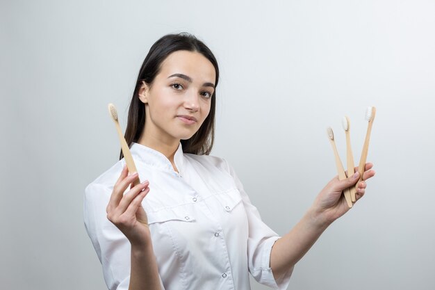 Une jeune fille brune tient une brosse à dents écologique dans ses mains. Une fille en blouse blanche prône le zéro déchet.