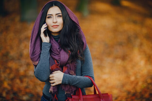 jeune fille brune utilisant son téléphone comme elle se promène dans le parc pendant l&#39;automne