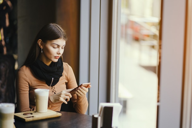 jeune fille brune en utilisant son téléphone tout en buvant un café dans un restaurant