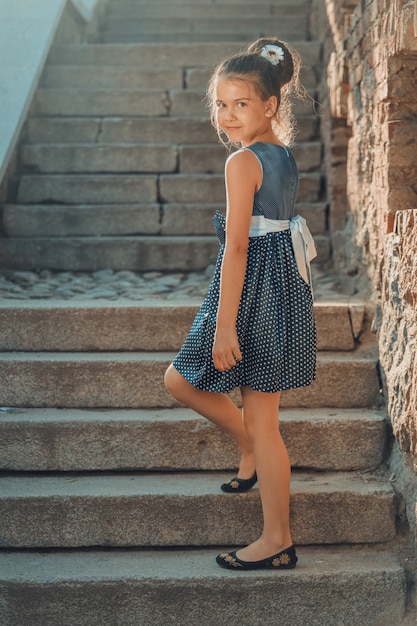 Une jeune fille brune vêtue d'une robe bleue à pois blancs descend les escaliers du parc. photo de haute qualité