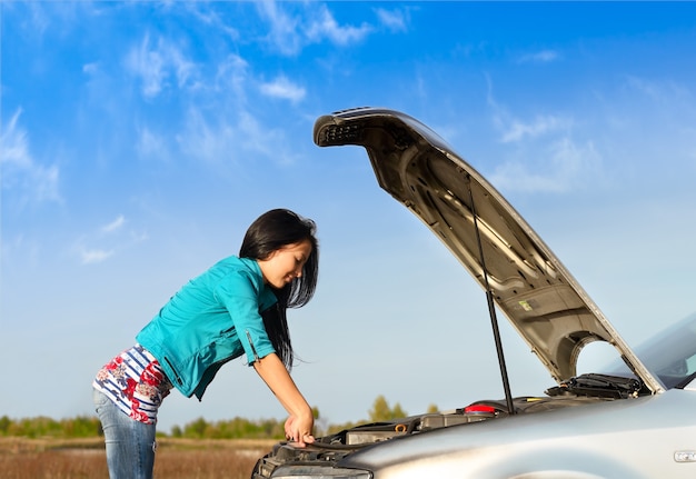 Jeune fille brune avec une voiture cassée avec capot ouvert