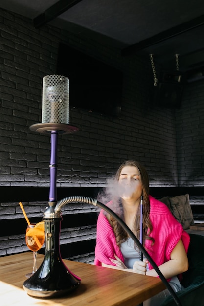 Jeune fille buvant de l'aperol Aperol spritz cocktail dans un verre La fille fume un narguilé Narguilé dans un restaurant Femme fume un narguilé et s'assied sur une chaise