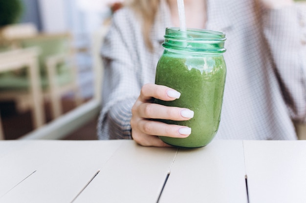 Jeune fille buvant un smoothie vert végétalien dans un café d'été