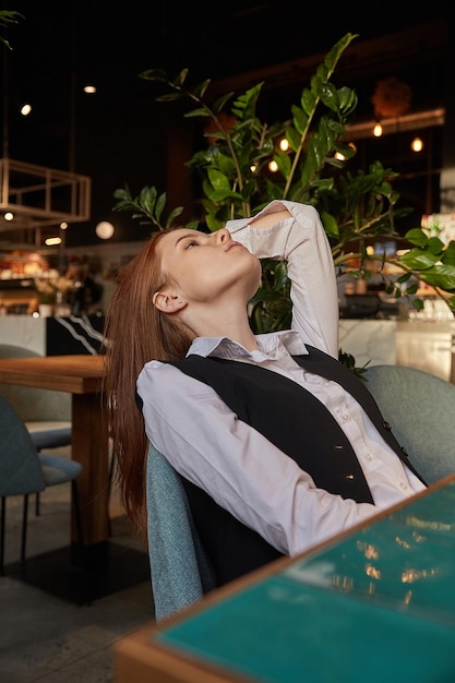 Jeune fille caucasienne aux cheveux longs allongée sur une chaise au café avec son menton vers le haut