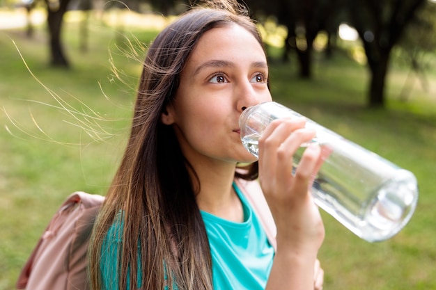 Jeune fille caucasienne buvant de l'eau d'une bouteille en verre au parc