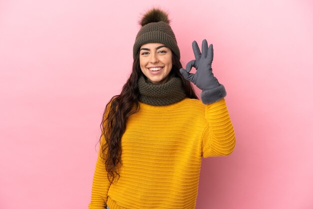 Jeune fille caucasienne avec chapeau d'hiver isolé sur fond violet montrant un signe ok avec les doigts