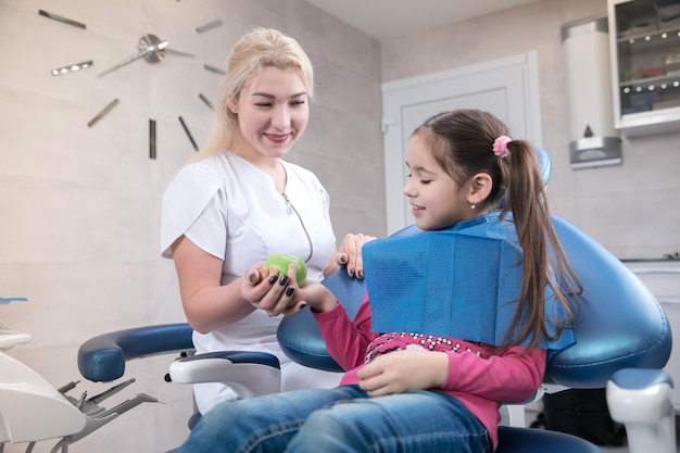 Jeune fille caucasienne avec des dents saines et un sourire heureux visitant le cabinet du dentiste pour la prévention de la cavité buccale. Enfant et médecin lors de l'examen. Concept de mode de vie sain, de soins de santé et de médecine.