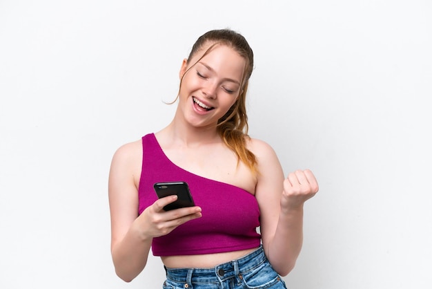 Jeune fille caucasienne isolée sur fond blanc avec téléphone en position de victoire