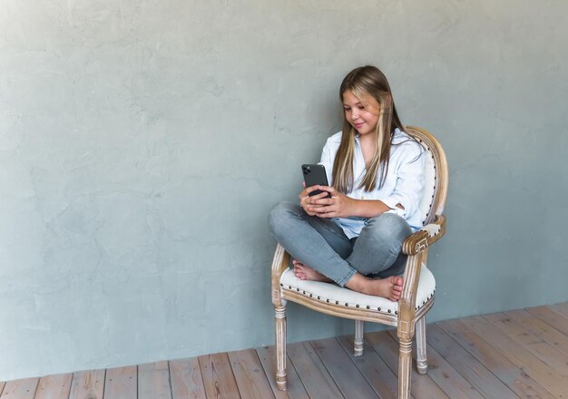 Jeune fille caucasienne à la peau bronzée et aux cheveux blonds utilisant des écouteurs sans fil pour appeler un ami via un smartphone tenant un téléphone portable