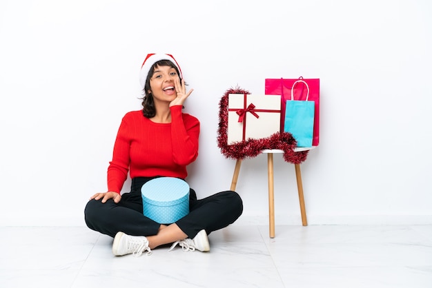 Jeune fille célébrant Noël assis sur le sol isolé sur blanc bakcground criant avec la bouche grande ouverte